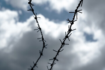 Fototapeta na wymiar Dark barbed wire lines on a dramatic grey blue sky background, captivity, jail or prison, labor or concentration camps abstract concept, nobody. Old barb wire with sharp edges, lack of freedom, fence