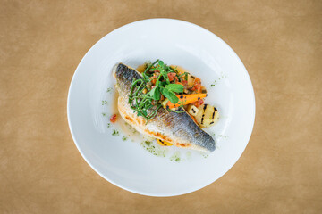 Top view of grilled sea bass fillets with mixed seasonal vegetables and garnish on a white plate...