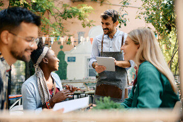 Happy waiter talking to black woman while taking her order in cafe,