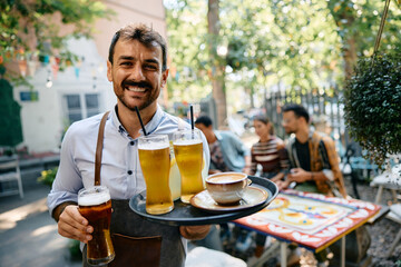 Happy waiter serving drinks while working in cafe and looking at camera.
