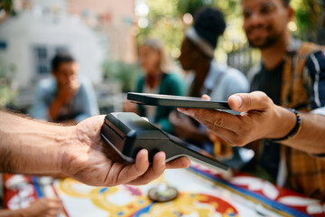 Close up of man using smart phone while paying to waiter in cafe.