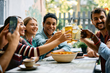Young happy people toasting with drinks while gathering in cafe,