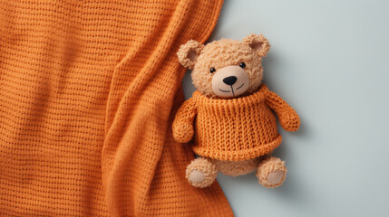 Fototapeta premium A small knitted amigurumi bear toy on an orange blanket, on a gray background. Flat lay, top view, copy space. space for text
