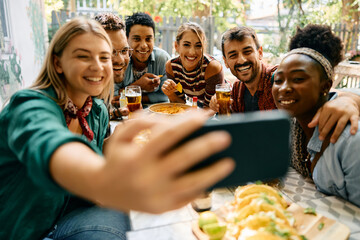 Happy friends having fun while taking selfie with cell phone in cafe.