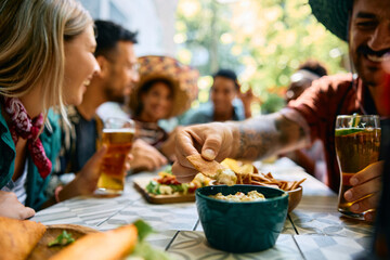 Close up of man dipping nacho chips in guacamole.