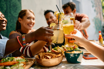 Close up of friends toasting with drinks while gathering in restaurant.