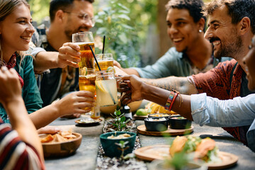 Close up of friends toasting with drinks while having lunch together in restaurant.