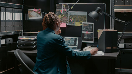 Police agent taking notes on case files in incident room, trying to solve criminal activity and catch suspect. Professional inspector examining research and surveillance photos. - obrazy, fototapety, plakaty