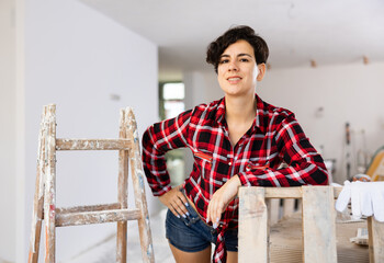 Pretty cottage owner in a plaid shirt and shorts posing in a room being renovated