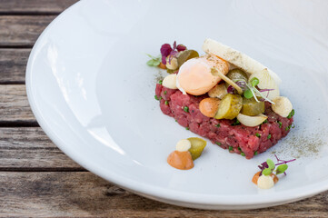 Close up of steak tartare with egg, toast and ingredients on white plate in restaurant