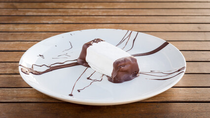 White marzipan biscuit dessert with butter cream, jam and chocolate on white plate on wooden table in restaurant
