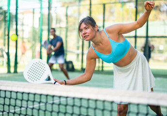 Caucasian woman in tank top and skirt playing padel tennis match during training on court.
