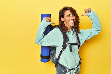 Woman with hiking backpack and mat on yellow feels proud and self confident, example to follow.