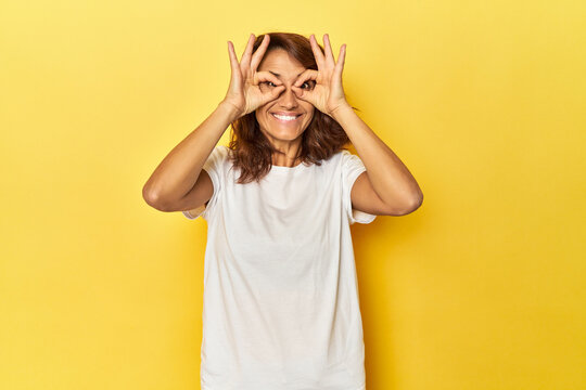 Middle-aged Woman On A Yellow Backdrop Showing Okay Sign Over Eyes