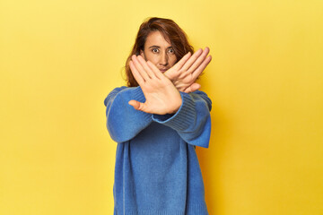Middle-aged woman on a yellow backdrop doing a denial gesture