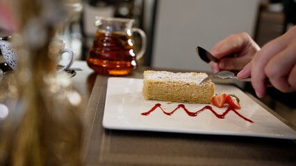 A metal fork and knife cut and thread a delicious piece of cake covered with powdered sugar, close-up, slow motion. Cheesecake is cut with a knife and fork, close-up.