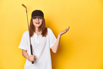 Redhead golfer with club and cap, studio shot receiving a pleasant surprise, excited and raising...