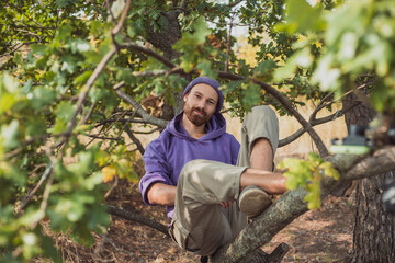 Young beaytiful guy laying lazy on the tree brunch in purple clothes
