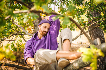 Young beaytiful guy laying lazy on the tree brunch in purple clothes