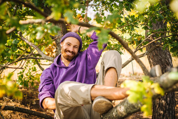 Young beaytiful guy laying lazy on the tree brunch in purple clothes