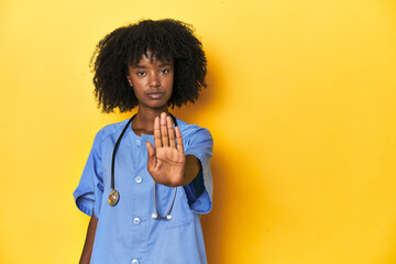 Young African-American nurse in studio with yellow background standing with outstretched hand...