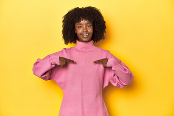 Obraz na płótnie Canvas Teen girl in pink sweatshirt, yellow studio backdrop surprised pointing with finger, smiling broadly.