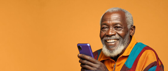 Portrait of smiling happy African senior man holding mobile phone on orange background, studio shot, wide banner with copy space for text