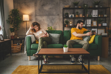 man and woman read book and use digital tablet at home on sofa bed