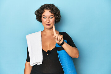 Athletic young woman with yoga mat showing number one with finger.
