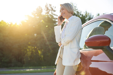Woman talking on mobile phone while standing on parking near her red car