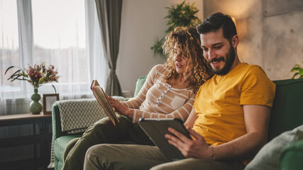 man and woman read book and use digital tablet at home on sofa bed