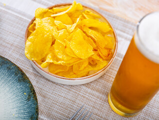 Appetizing snack of potato chips with a glass of foamy beer. Close-up image