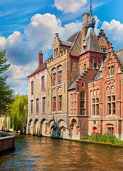 Medieval town Bruges in Belgium. Panorama and landscape vintage channel with old bruges brick houses broach on roof. Sunny day Brugge blue sky, clouds green trees. Europe travel destination