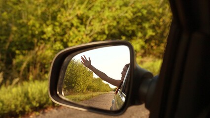 Happy travel woman enjoy freedom summer road trip with hand in window back mirror reflection view. Smiling female tourist in driving automobile exploration adventure bright sun light with green trees