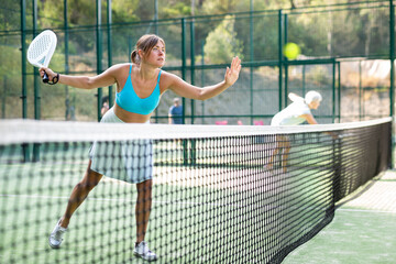 Portrait of sporty young woman playing padel on open court on summer day, ready to hit ball. Sport...