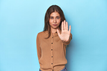 Teen girl in brown polo shirt on blue standing with outstretched hand showing stop sign, preventing...