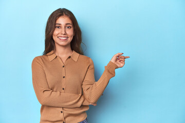 Teen girl in brown polo shirt on blue smiling cheerfully pointing with forefinger away.