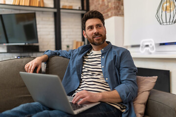 Young bearded handsome man sitting at home and working on laptop