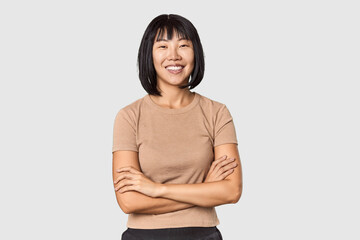 Young Chinese woman posing on studio background who feels confident, crossing arms with...