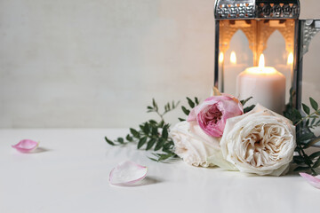 Burning silver Moroccan, Arabic lantern with pink roses flowers and green leaves on white table....