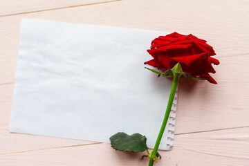 Red rose and white mockup paper blank on wooden background. Flat lay, top view, copy space. Valentine's Day or Mother's Day greeting card