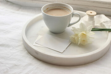 Breakfast still life. Cup of latte coffee, bouquet of narcissus, daffodil flowers on marble tray....