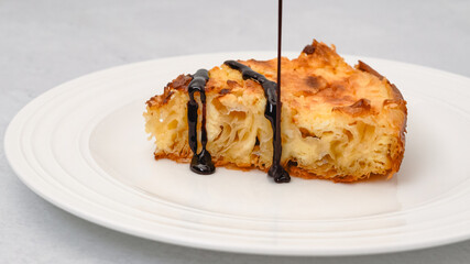 Slice of phyllo dough pie with cream cheese filling and chocolate sauce topping close-up on a white plate