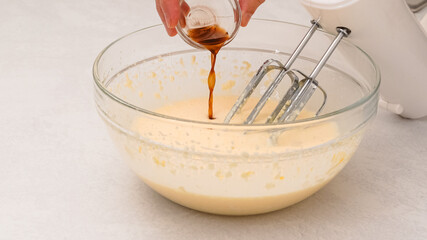 Chef hands delicately pour vanilla extract into a bowl, baking process in motion