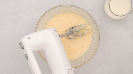 Ingredients like cream cheese, eggs, whipped cream, and powdered sugar mixed with a mixer