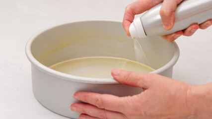 Woman's hands delicately coat a baking pan with oil spray, close-up