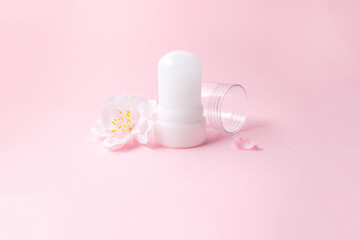 Crystal deodorant surrounded by flowers on pink background. Mineral eco personal care product concept. Selective focus, copy space