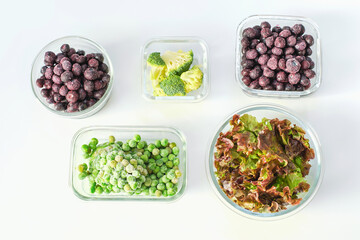 Green vegetables and berries in glass lunch boxes on white background close-up, top view.
