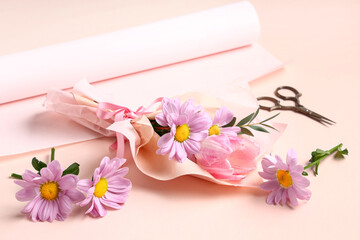 Obraz na płótnie Canvas Mini bouquet of beautiful spring flowers in wrapping paper with scissors on pink background. International Women's Day