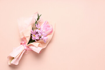 Mini bouquet of beautiful spring flowers in wrapping paper on pink background. International Women's Day